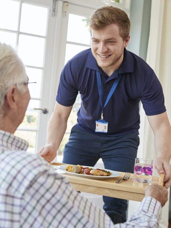 Male care worker serving dinner to a senior man at his home